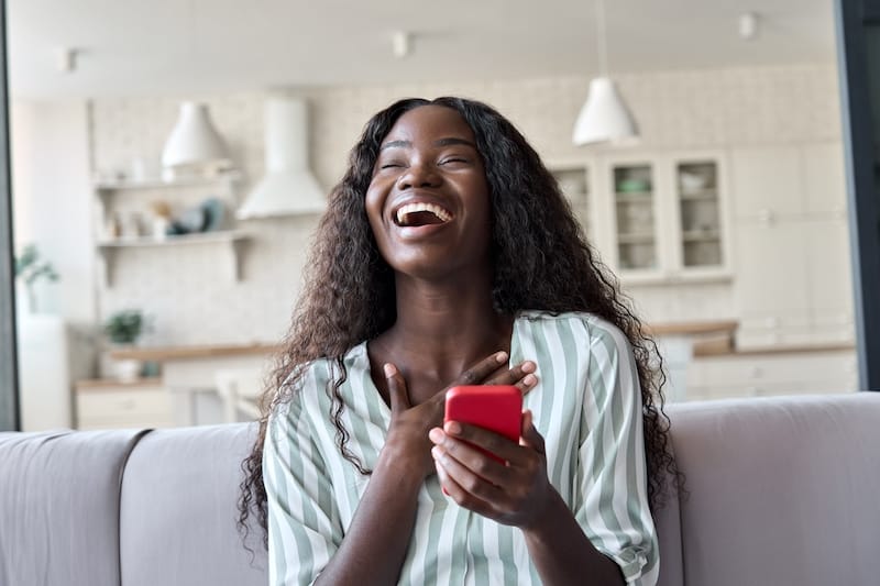 paragraphs for her black african woman laughing on sofa reading text message